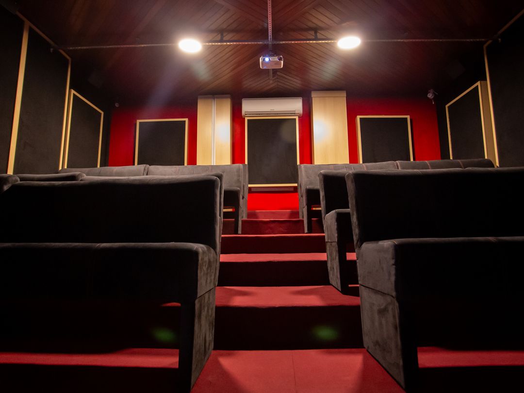 Sala de cinema do Estúdio A com fileiras de sofás, carpete vermelho e luzes de teto