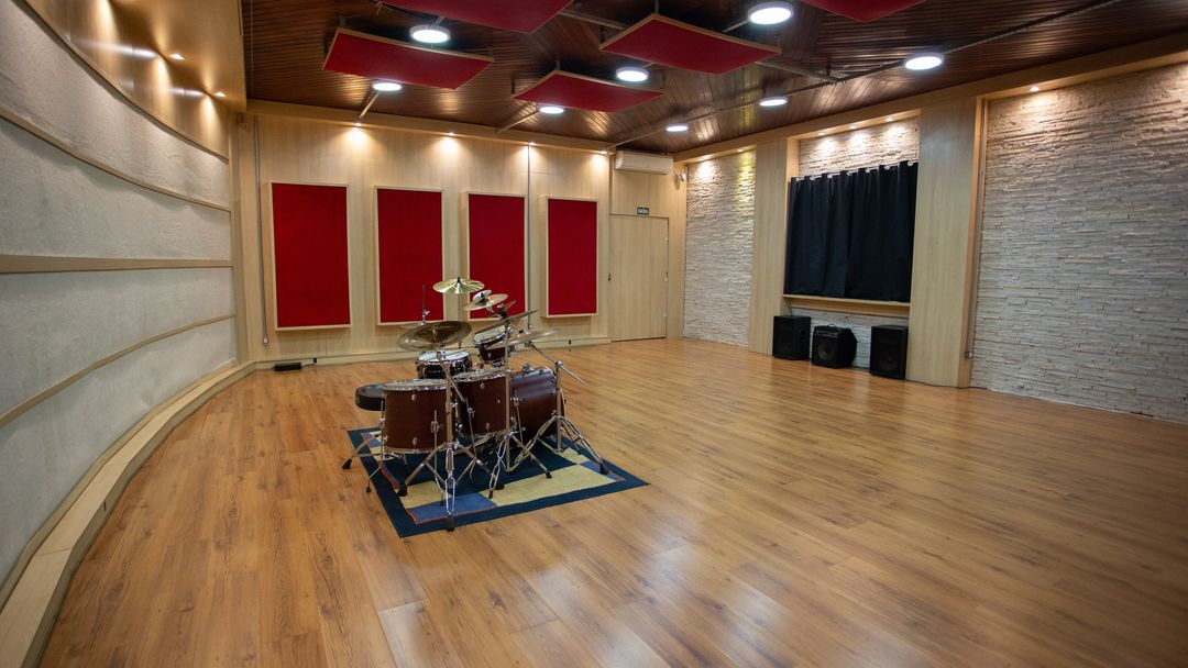 Bateria montada no centro da sala de gravação do Estúdio A, com painéis acústicos vermelhos e piso de madeira