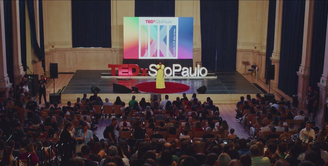 Palco de um evento TEDx com as letras vermelhas e a plateia cheia