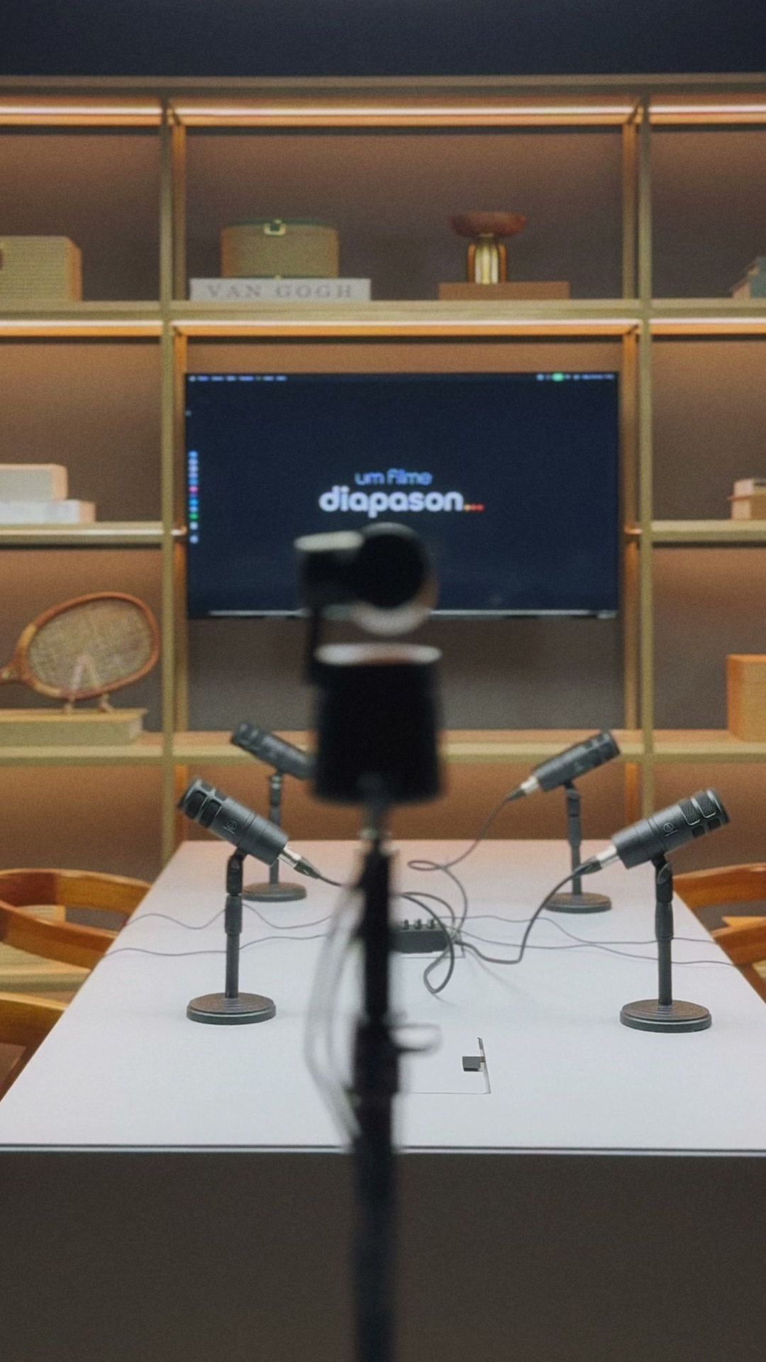 Câmera PTZ em primeiro plano diante da mesa de podcast do Estúdio B · M8