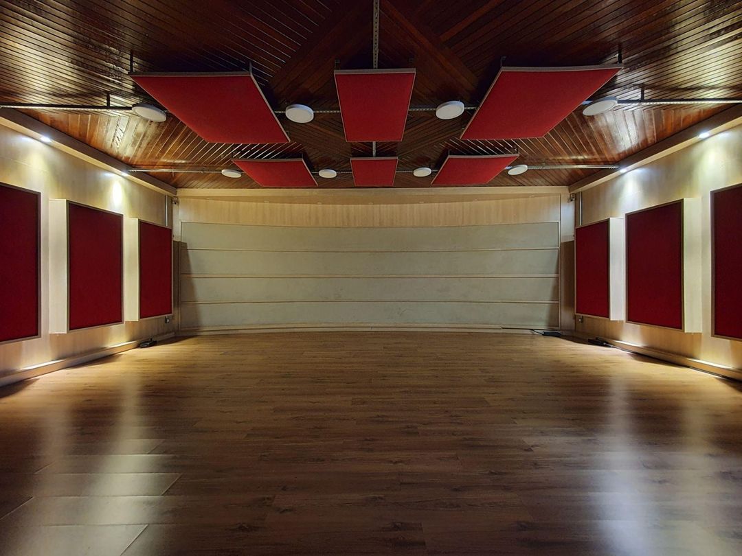 Sala de gravação do Estúdio A vazia, com piso de madeira e painéis acústicos