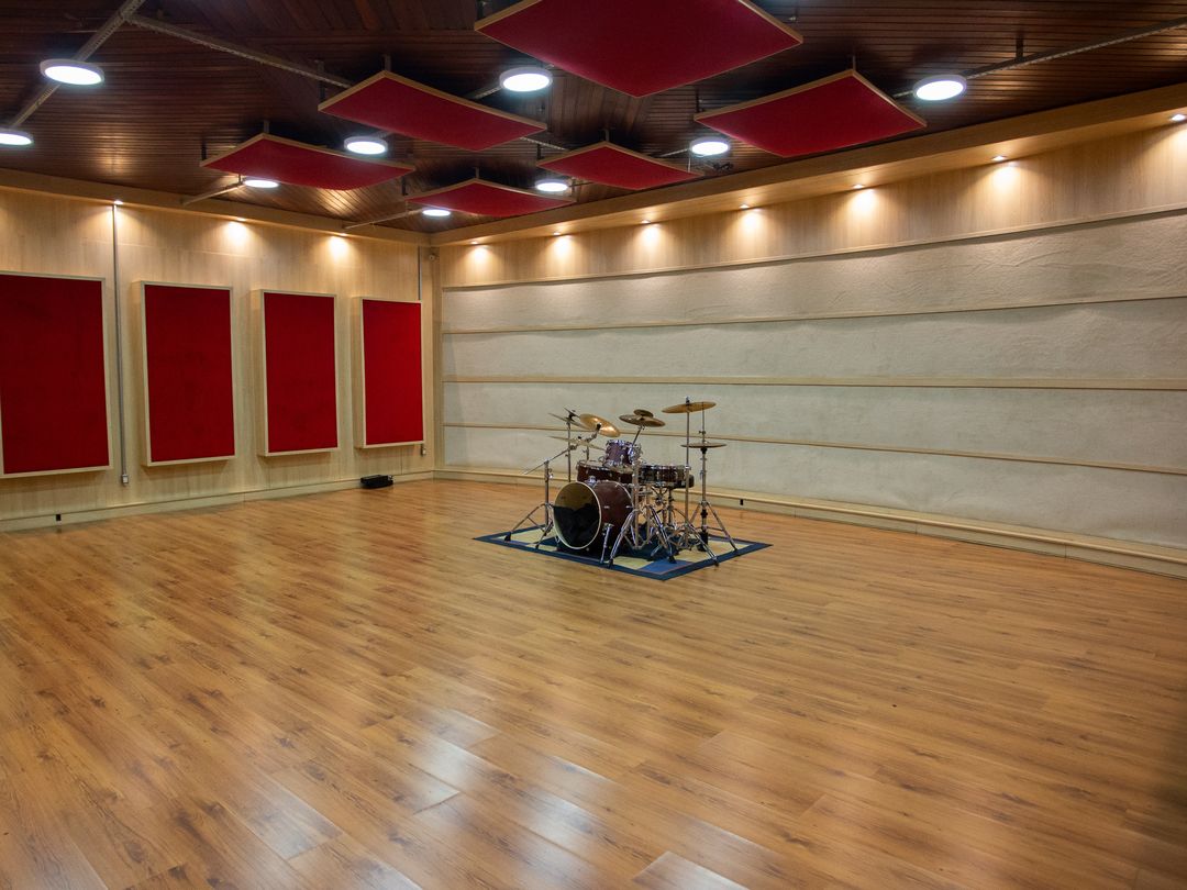 Sala de gravação do Estúdio A, ampla, com piso de madeira, painéis acústicos vermelhos e uma bateria no centro