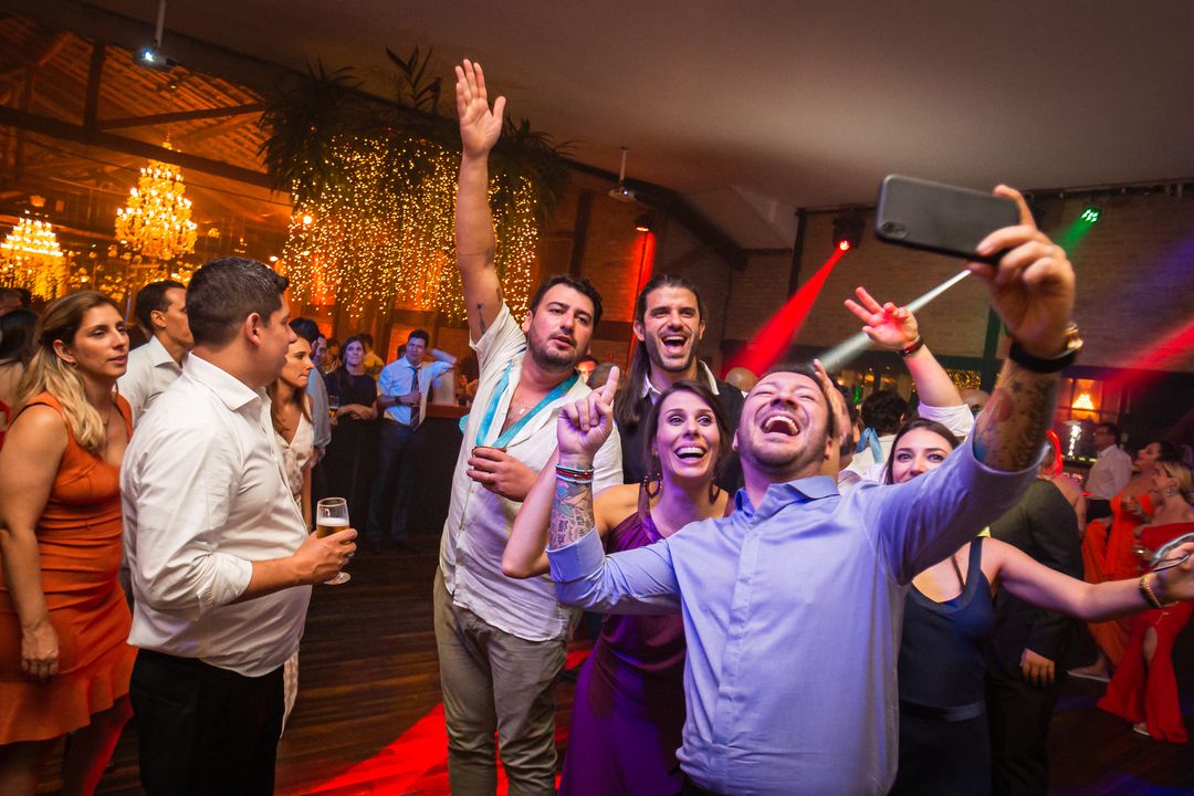 Convidados pulando de braços para cima na pista de dança, sob uma cortina de luzinhas douradas