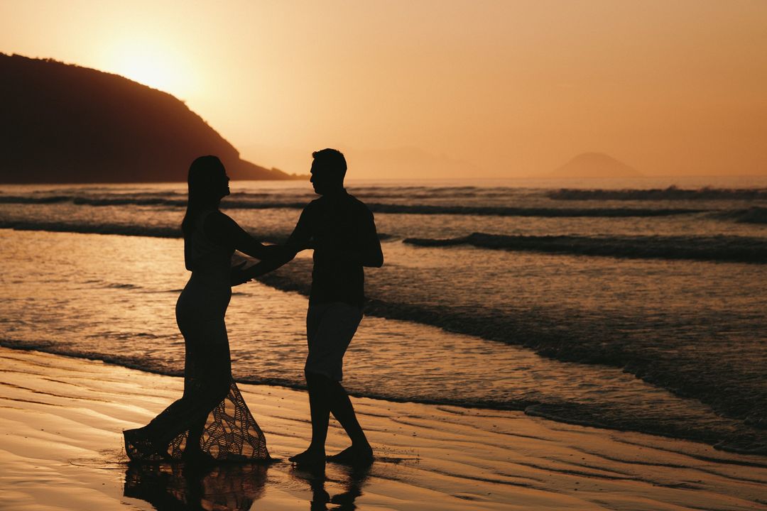 Silhueta de um casal dançando na praia ao pôr do sol, em ensaio pré-wedding