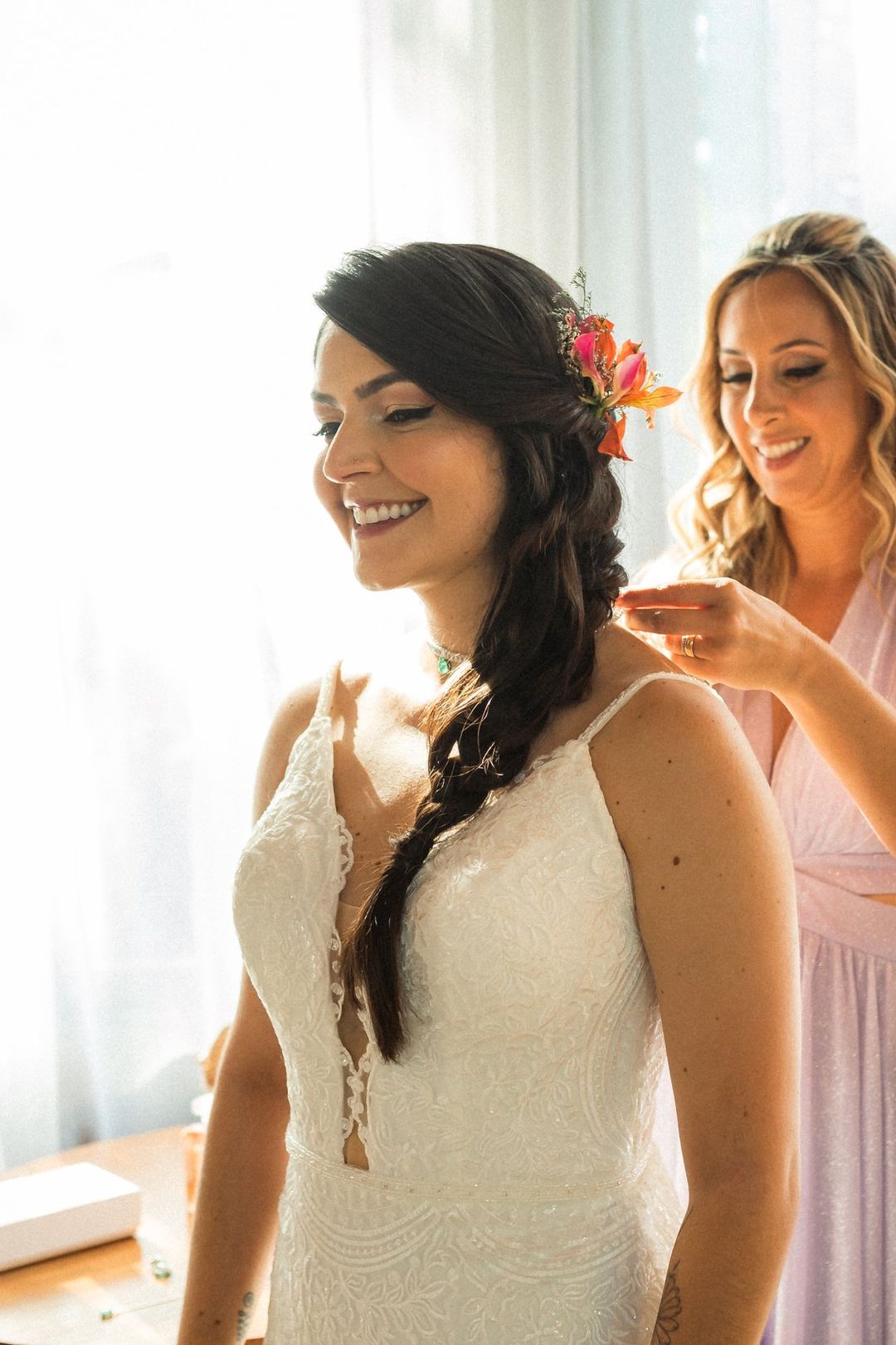 Noiva sorrindo no making of, com uma flor no cabelo